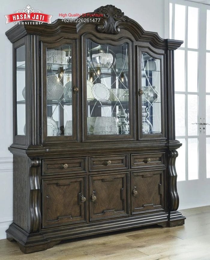 Tampilan penuh lemari hias jati mewah seri Maylee 3 pintu kaca warna cokelat gelap dihiasi pajangan cangkir porselen di dalam ruang makan produk Hasan Jati Furniture.