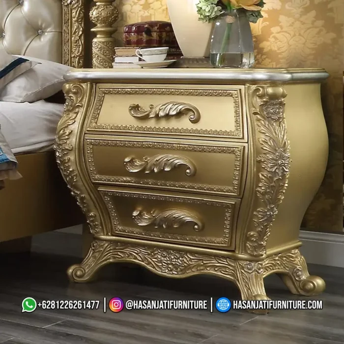 Meja nakas lampu tidur dengan profil laci cembung dan kaki lengkung berukir warna emas dari set kamar mewah seri Eastern produk Hasan Jati Furniture.
