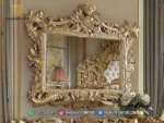 Bingkai cermin dinding gantung dengan ukiran mahkota rimbun warna emas mewah seri Bernadette memantulkan visual dipan kasur produk Hasan Jati Furniture.