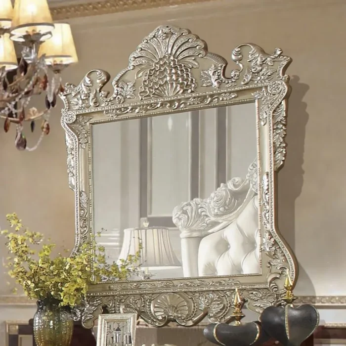 Bingkai cermin dinding gantung ukir mewah tipe Vatican warna champagne silver memantulkan interior sandaran kasur produk Hasan Jati Furniture.