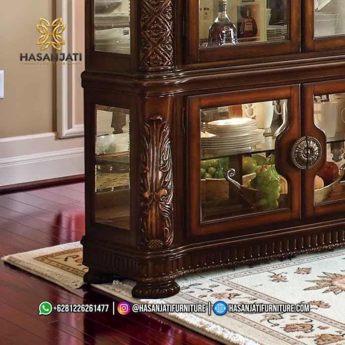 Detail pintu kaca bagian bawah lemari jati Vendome dengan tarikan kuningan bulat besar medallion dan struktur kaki decorative bun feet.