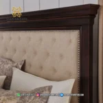 Close up sandaran kepala atau headboard tempat tidur Brynhurst memperlihatkan detail empuk jok kain beige motif kancing tanam dan list paku payung kuningan produk Hasan Jati Furniture.