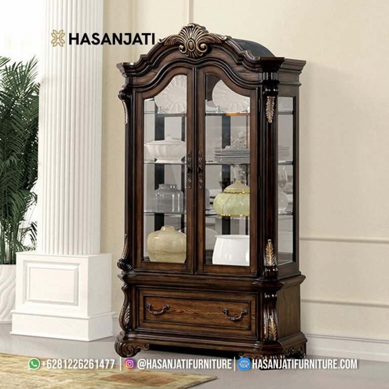 Tampilan penuh lemari hias jati mewah seri Leovanni 2 pintu kaca warna cokelat gelap kombinasi ukiran emas di samping pilar ruang keluarga produk Hasan Jati Furniture