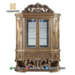 Tampilan penuh tepat dari depan lemari hias jati mewah seri Constantine 2 pintu kaca warna cokelat emas berlatar putih polos produk Hasan Jati Furniture.