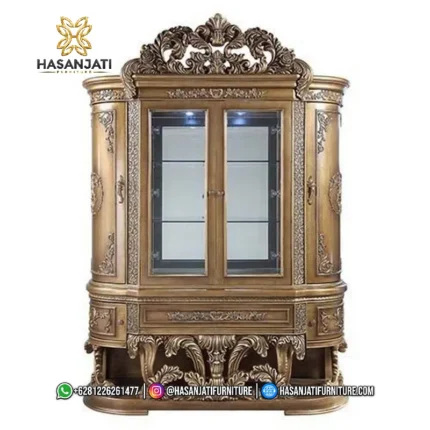 Tampilan penuh tepat dari depan lemari hias jati mewah seri Constantine 2 pintu kaca warna cokelat emas berlatar putih polos produk Hasan Jati Furniture.