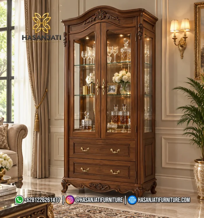 Tampilan penuh lemari hias jati mewah seri Cordelia 2 pintu kaca dan 2 laci bawah warna cokelat antik dihiasi lampu di dalam ruang tamu produk Hasan Jati Furniture.