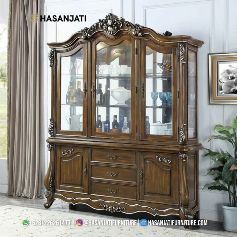 Tampilan penuh lemari hias jati mewah seri Latisha 3 pintu kaca warna cokelat antik dihiasi pajangan cangkir porselen di dalam ruang tamu produk Hasan Jati Furniture.